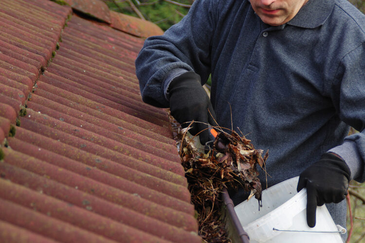 Man performing gutter maintenance and cleaning out a clogged gutter.